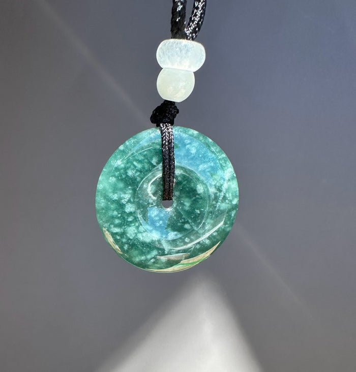 Blue Green stone pendant on a black cord against a gray background