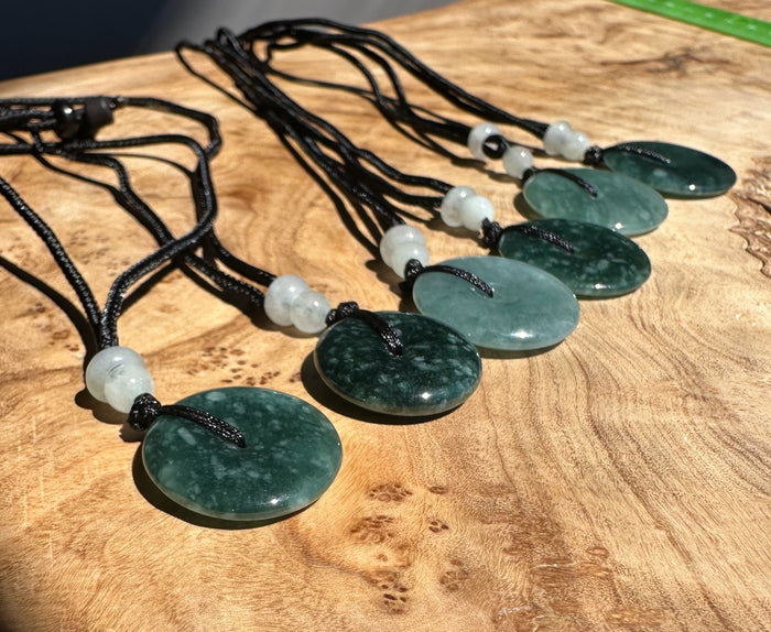 Blue Green jadeite pendants on black cords arranged on a wooden surface