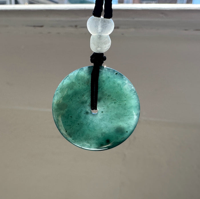 Blue Green jadeite pendant with two white beads on a string against a neutral background