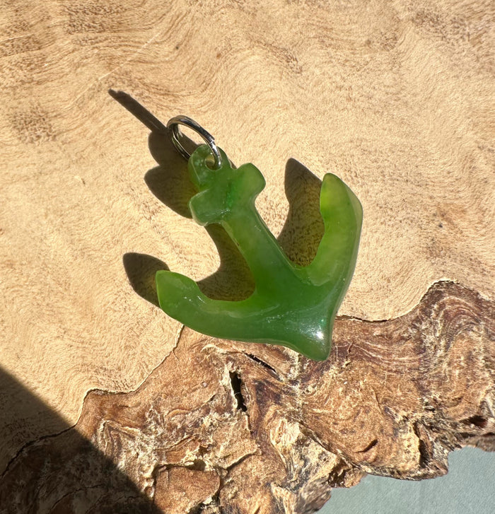 Green jade anchor charm with a silver jump ring on a rustic wooden surface.