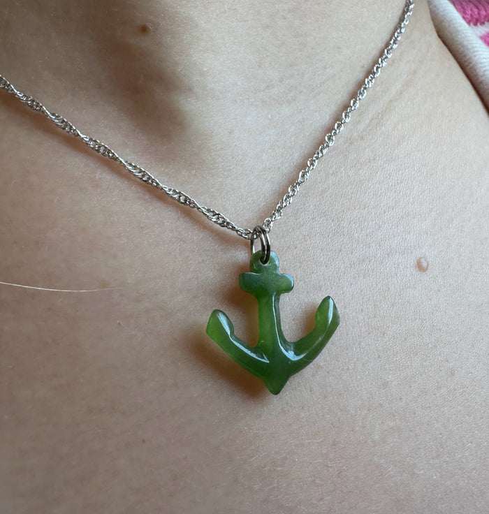 A close-up of a person wearing a silver chain necklace with a green anchor-shaped pendant.