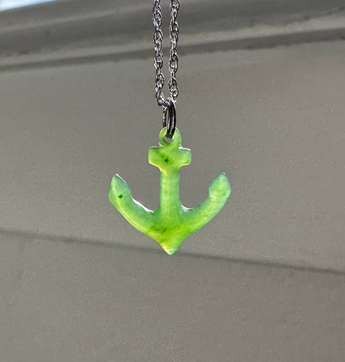 Bright green jade anchor pendant on a silver chain against a neutral background.
