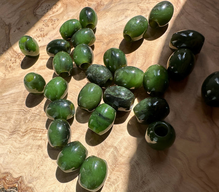 Green jade barrel beads 15x12mm with center holes scattered on a wood surface