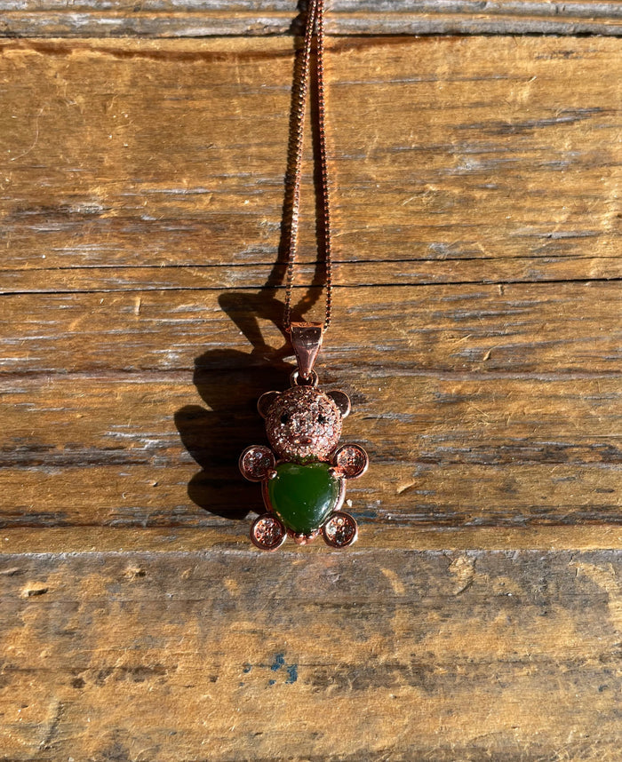 Rose gold bear pendant with crystal head and green jade body on a chain displayed on a wooden surface