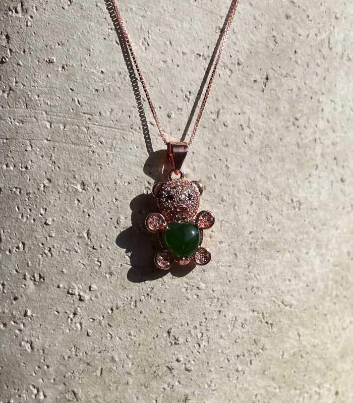 Jade bear pendant on a rose gold chain against textured concrete background showing the green jade body