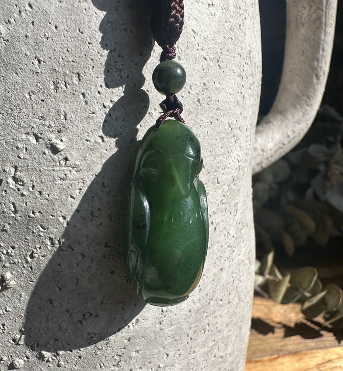 34mm Jade bird pendant hanging on a dark cord against a textured stone surface.