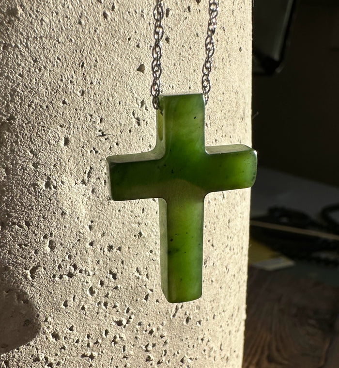 Jade cross pendant 30mm hanging from a silver chain against a textured light wall