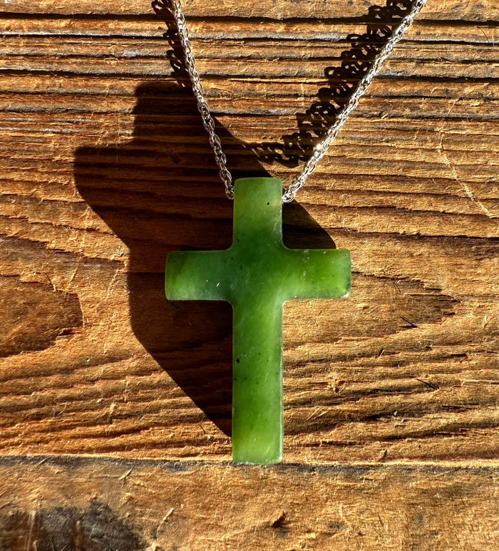 Jade cross pendant 30mm resting on wood with a silver chain draped above