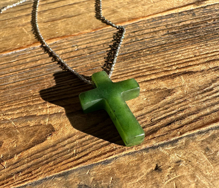 Green jade cross pendant 30mm on a silver chain laid on wood with sunlight