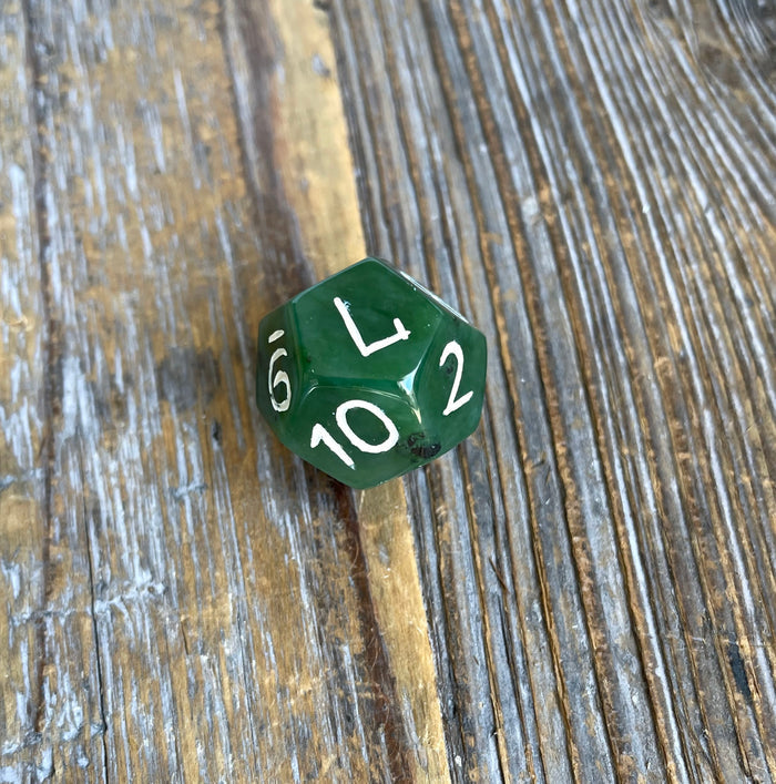 Green jade D12 die tilted on a rustic wooden surface with white numbers visible