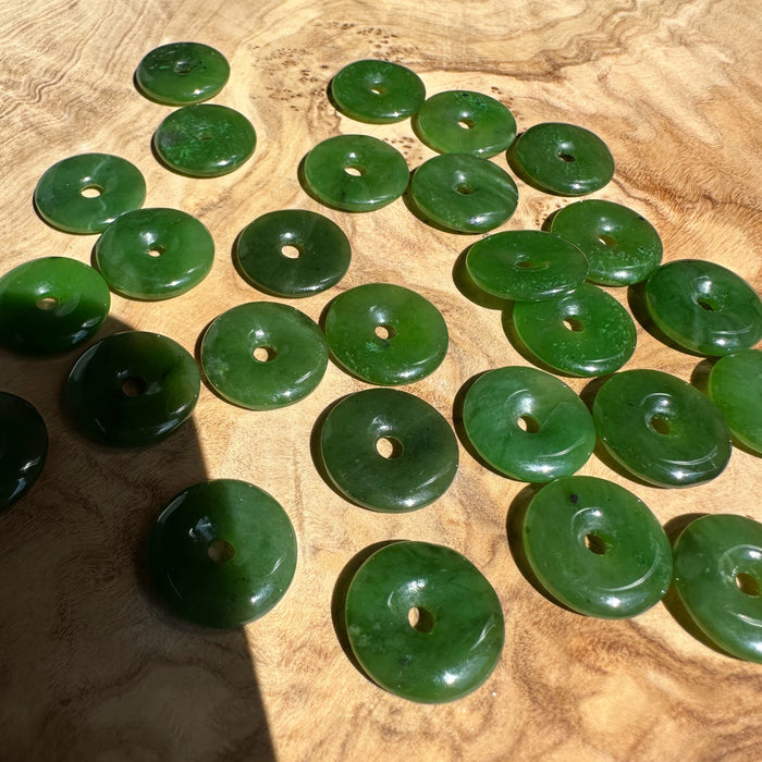 Green jade donut beads with central holes scattered on a wooden surface