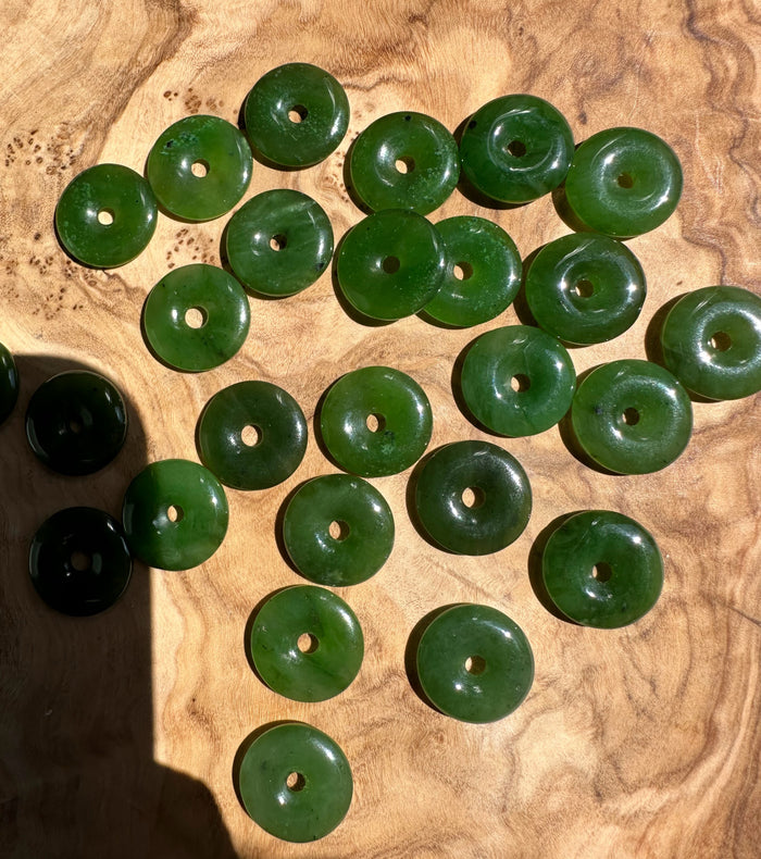Group of green jade donut beads with center holes arranged on a wooden surface