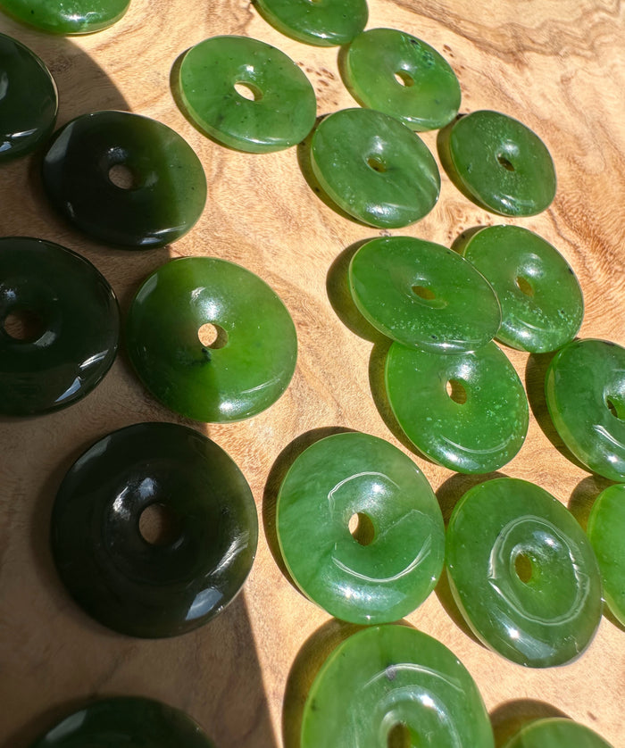 Green jade donut beads in various shades scattered on a warm wooden surface.