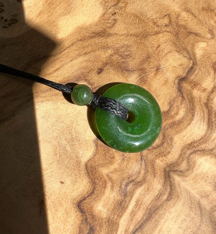 Green jade donut pendant with a small bead on a black cord necklace.