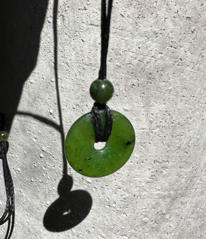 Green jade donut pendant on a black cord with a small round bead.