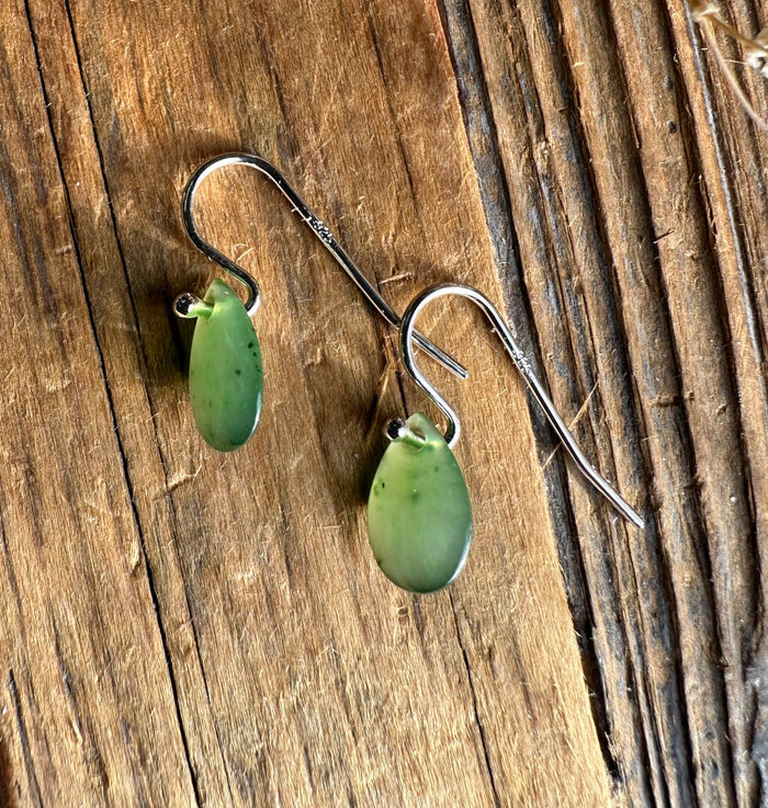 Green jade teardrop earrings with silver hooks on a rustic wooden surface