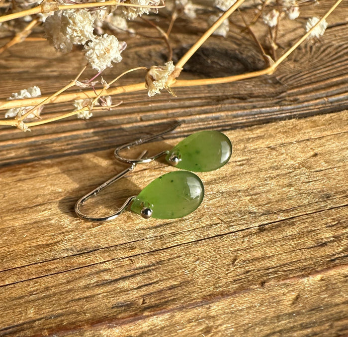 Jade teardrop earrings with silver hooks on a rustic wooden surface with dried flowers