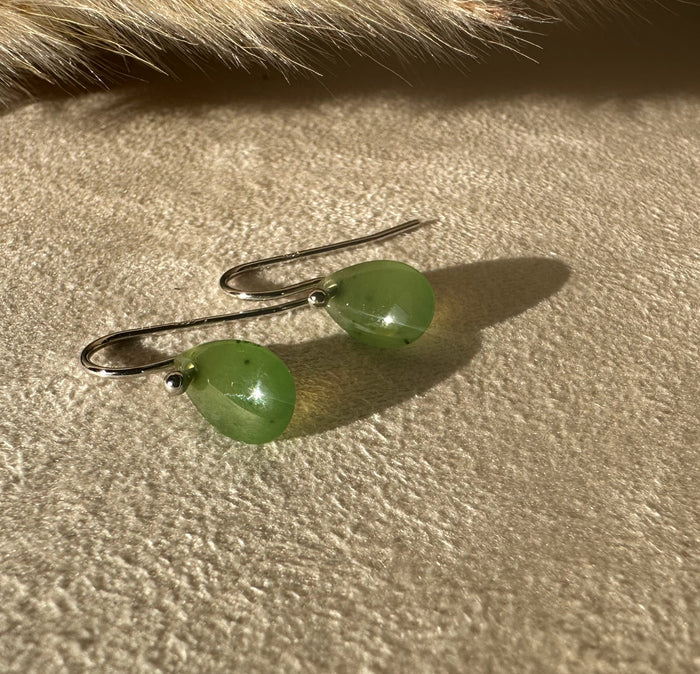 Jade teardrop earrings on a beige textured fabric with warm sunlight and shadows