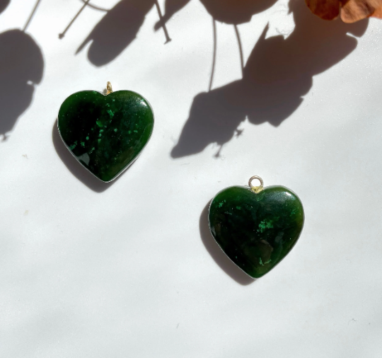 Two jade heart charms with gold loops on a white background