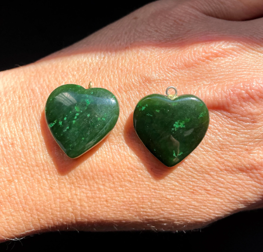 Two jade heart charms with metal loops resting on a hand in bright light