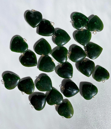 Assorted jade heart charms with small metal loops scattered on a white background