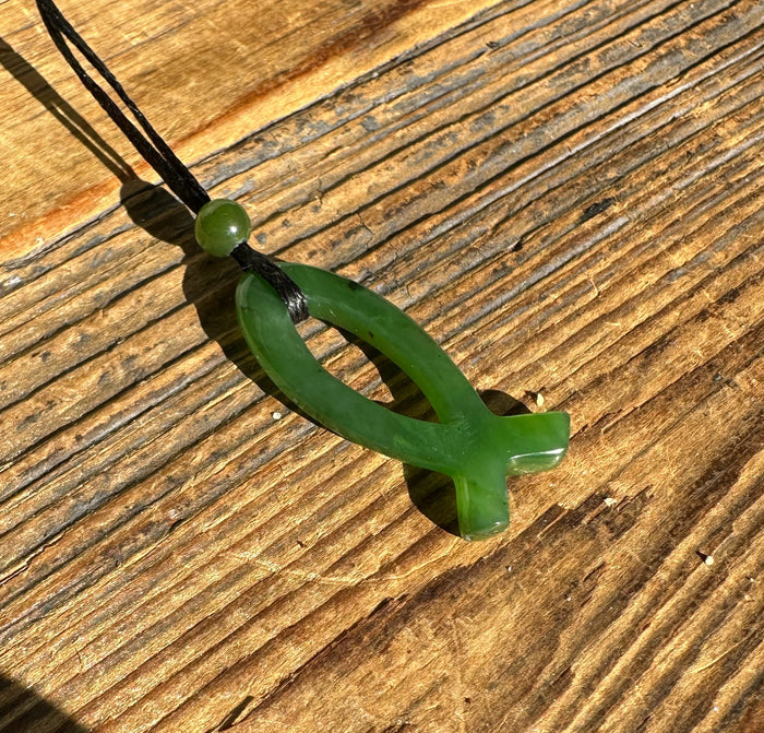Green jade Ichthys pendant shaped like a fish on a black cord with a small green bead.