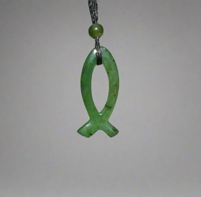 Green jade Ichthys pendant 30mm on a black cord with a round bead above against a gray backdrop.