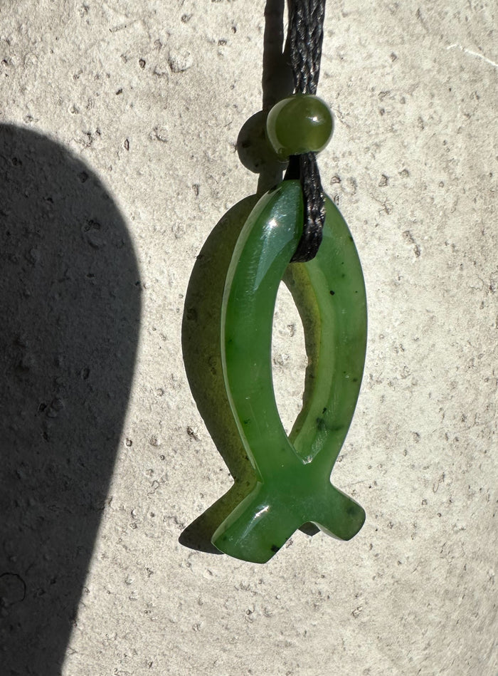 Close up of 30mm green jade Ichthys pendant with oval loop and cross tail on a black cord.