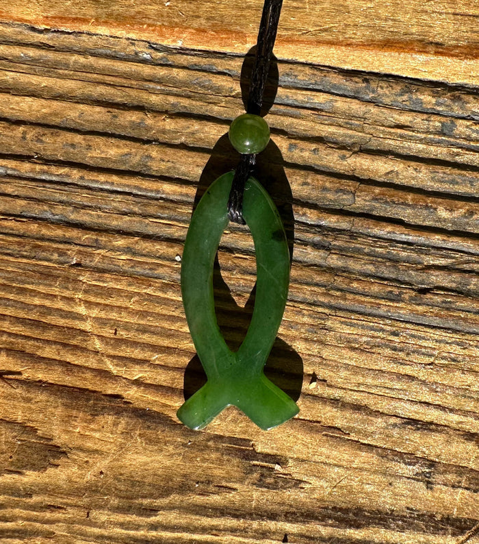 Green jade Ichthys pendant on black cord with a round bead against a wooden surface