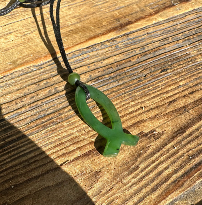 Close up of green jade Ichthys pendant threaded on a black cord with a round bead