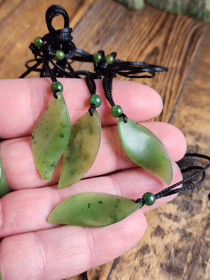 Three pale green jade leaf pendants on black cords with small green beads