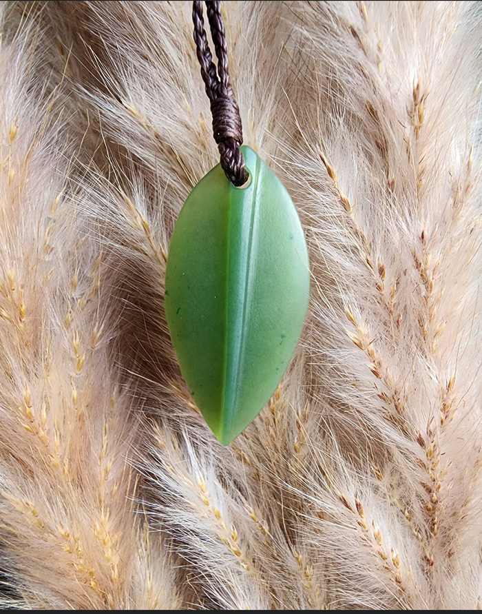 Green jade leaf pendant on a braided brown cord against dried grasses.