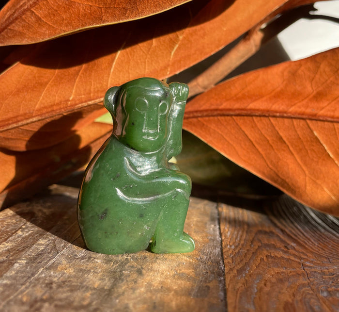 Green jade monkey figurine 1.9 inches resting on a weathered wooden surface with orange autumn leaves in the background.