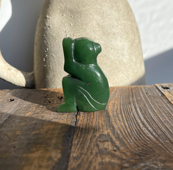 Side view of a green jade monkey figurine 1.9 inches on a rustic wooden surface.