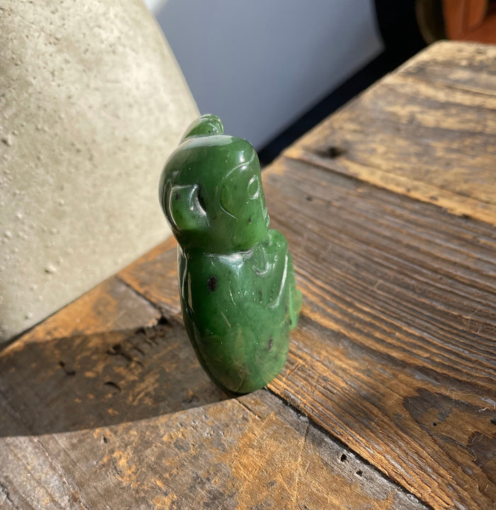 Back view of a green jade monkey figurine 1.9 inches on a weathered wooden surface.