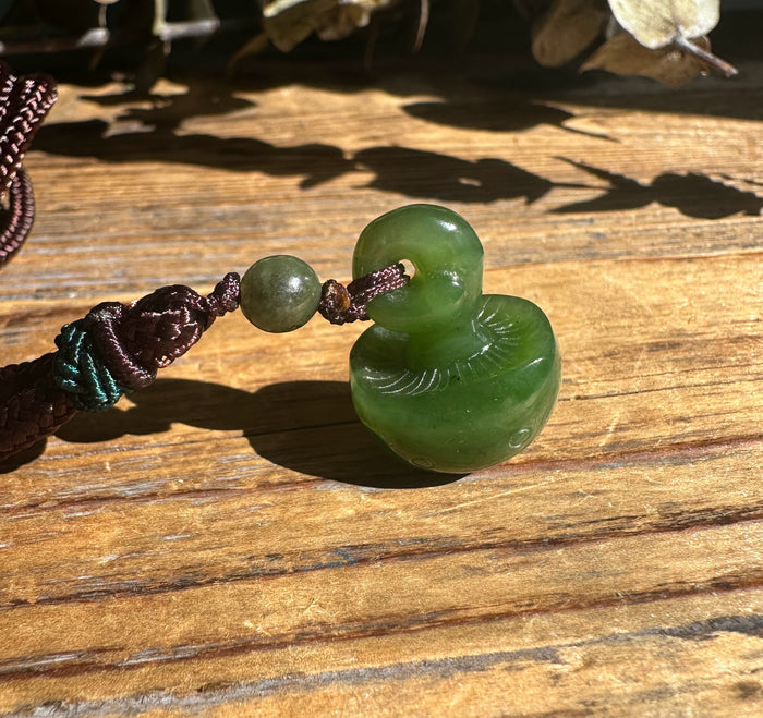 Green jade mushroom pendant with a donut shaped ring on a braided cord resting on a wooden surface