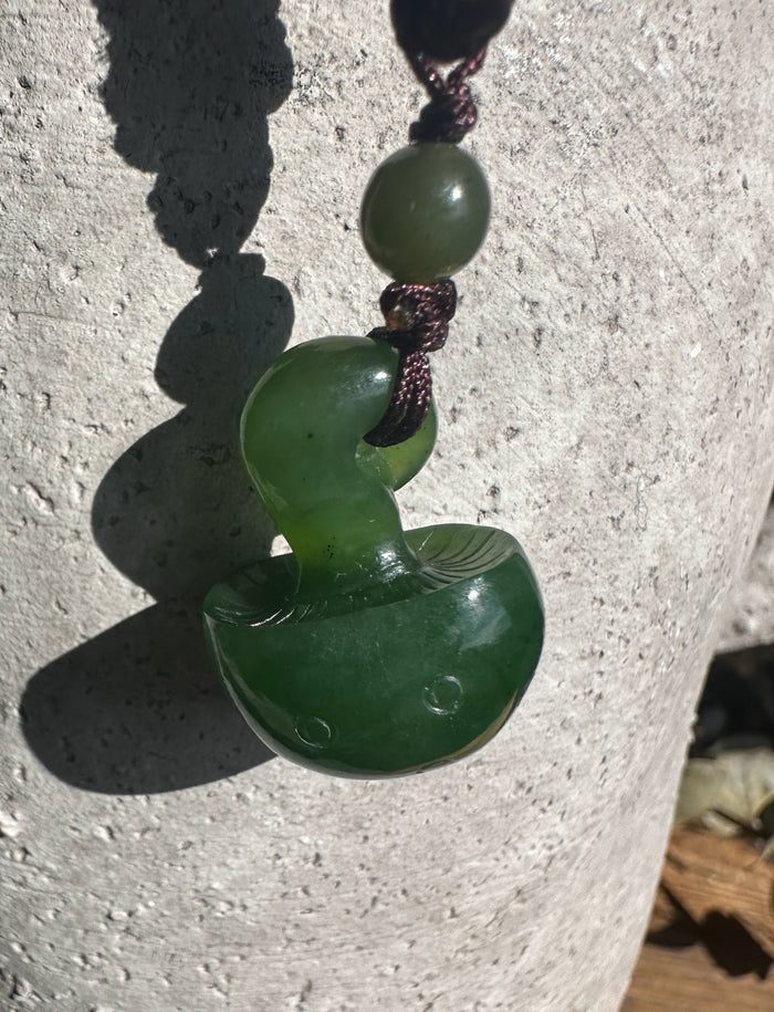 Close up of a green jade bead above a curved mushroom pendant on a brown braided cord