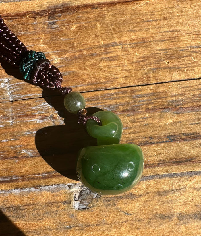 23mm Jade mushroom pendant on a dark braided cord with a green bead, set on wood.