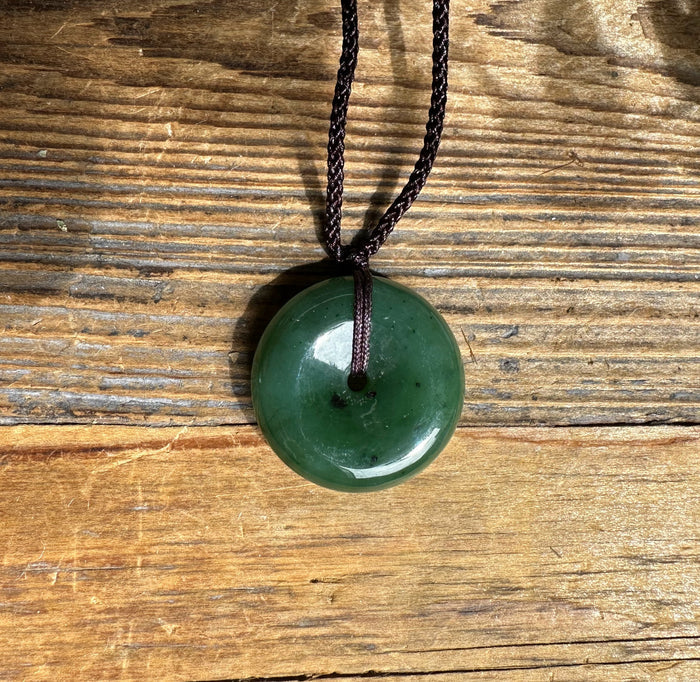 Dark green jade donut pendant on a brown nylon cord resting against a rustic wooden surface