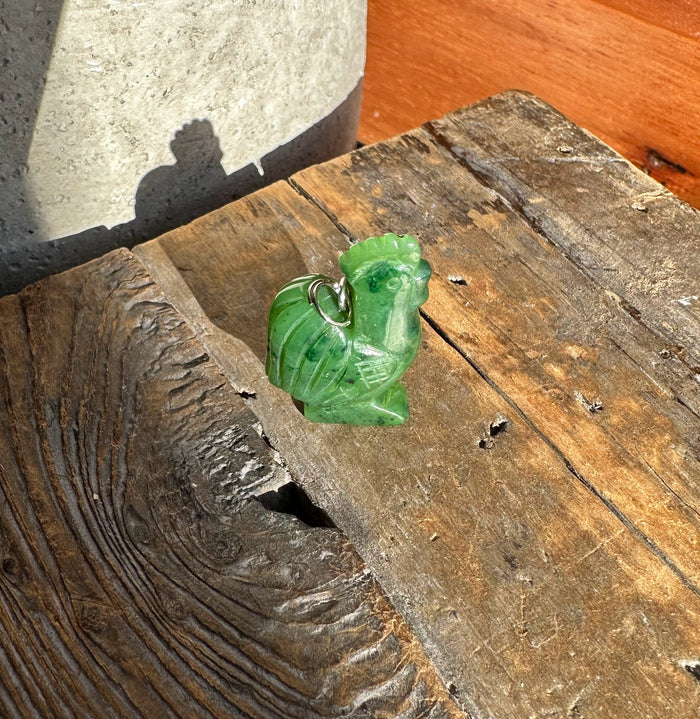 Green jade rooster pendant on a silver chain against weathered wood