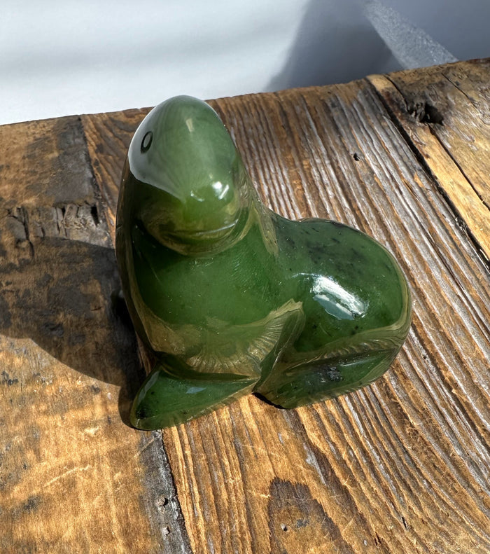 Side-angle view of a jade seal in a rounded animal shape resting on a weathered wooden surface