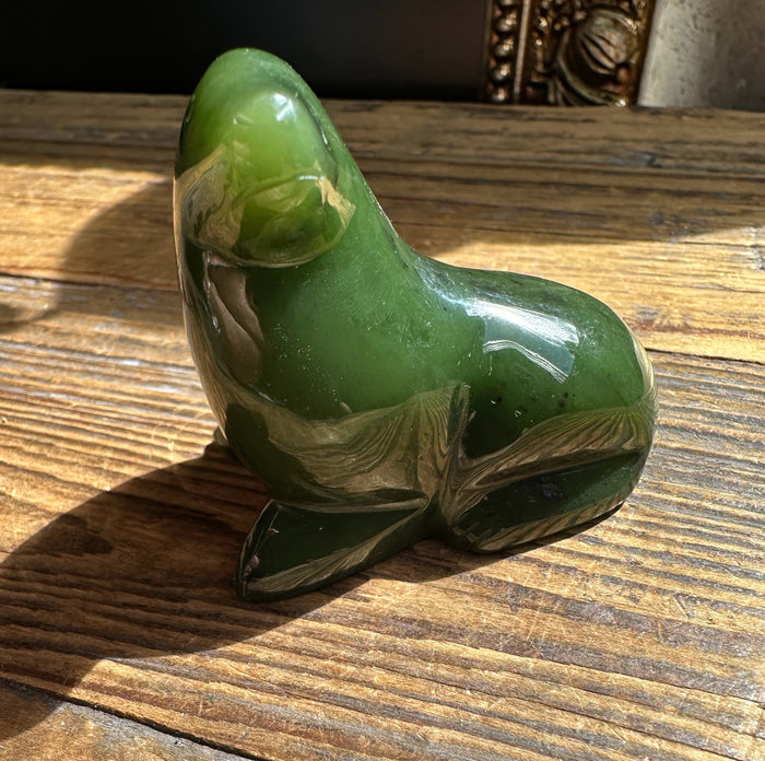 Green jade seal sculpture of a seated seal resting on a wooden surface