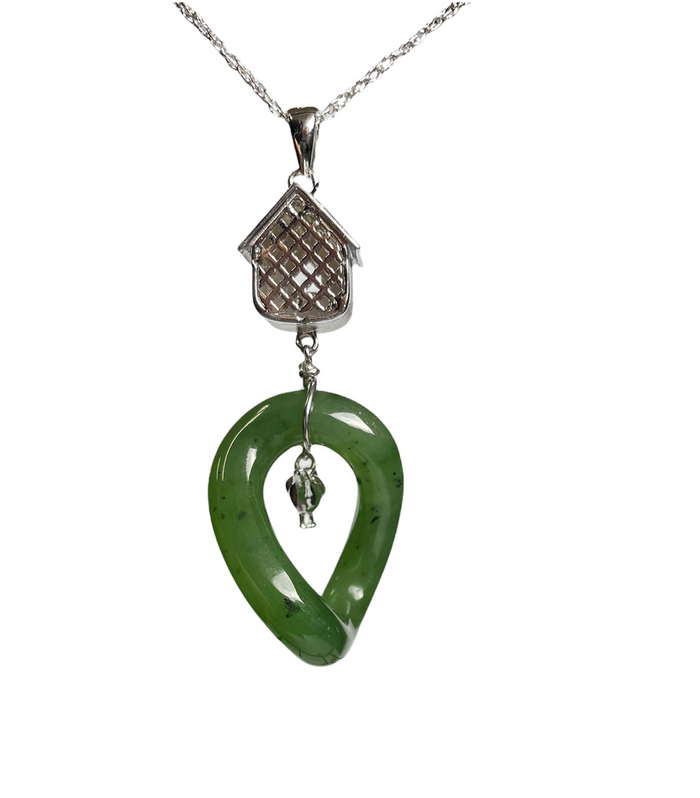Close up of silver birdhouse pendant above a green jade loop pendant on a chain against a white background.