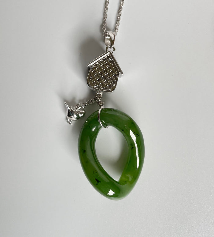 Jade green oval loop hangs from a silver birdhouse pendant with lattice front and a tiny bird charm.