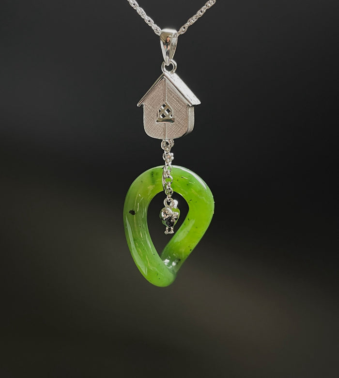 Jade green oval pendant with a silver birdhouse charm above and a floral accent at the bottom.