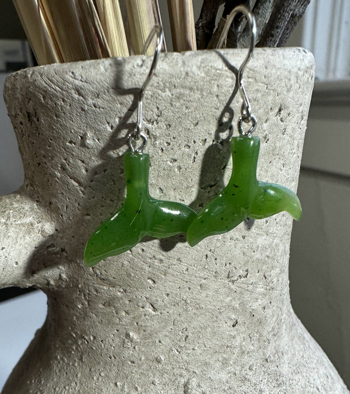 Jade whale tail earrings in vivid green with silver hooks displayed against a textured stone backdrop