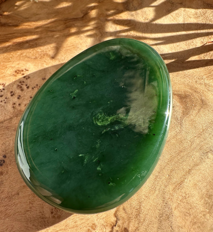 Polished oval green jade worry stone on a tan fabric background.