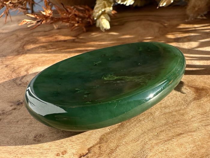 Green jade worry stone in a smooth oval shape resting on a wooden surface with dried plants in the background