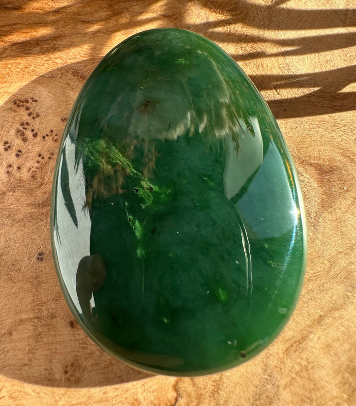 Top view of a glossy green jade worry stone with an oval shape resting on a wooden surface