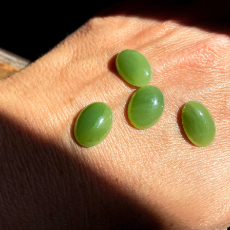 Four light green Canadian jade cabochons on a sunlit hand